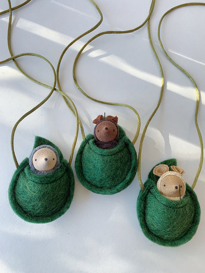 Fairy Shadow Critter Necklaces, angled view of all three styles on a white surface, showing grey mole, chocolate mouse, and beige mouse knitted critter figures nestled in open felted green wool pouches with gold metallic cord straps
