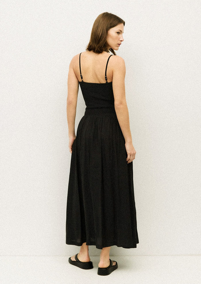 A woman wearing a black spaghetti strap dress with fitted bodice.