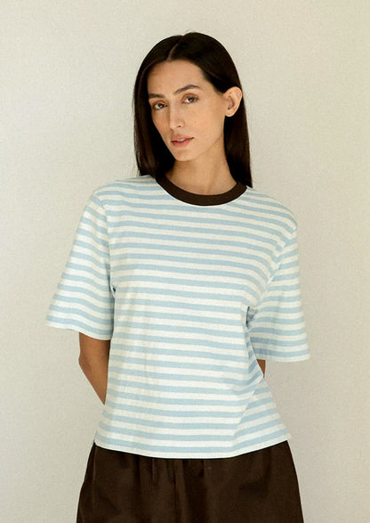 Woman wearing a light blue and white striped shirt against a plain background