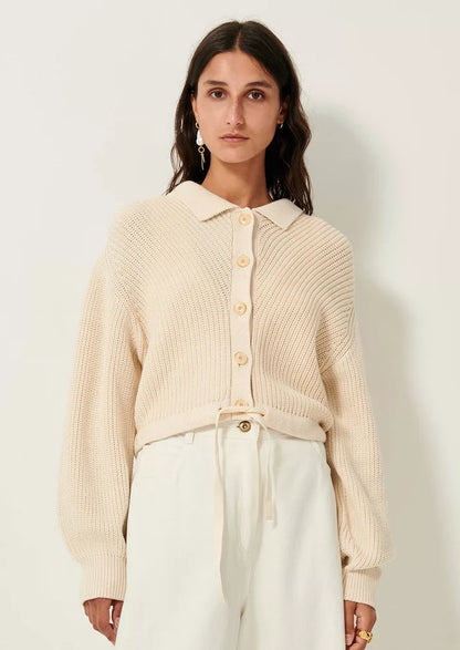 A woman wearing a cream knit sweater with collar, button front and tie waist.