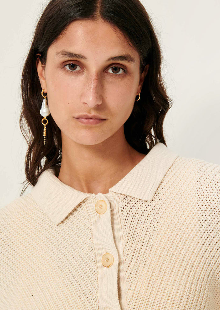 A woman wearing a cream knit sweater with collar, button front and tie waist.