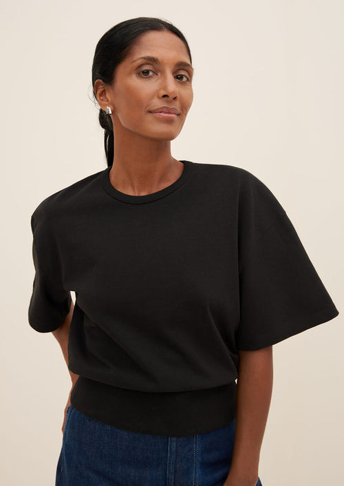 A woman wearing a boxy tee with short sleeves and fitted ribbed waistband, in black.