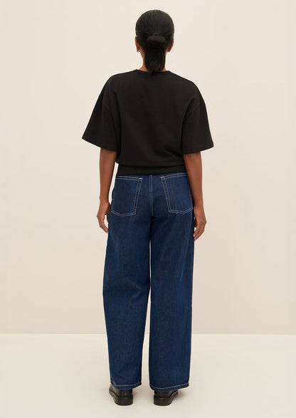 A woman wearing a boxy tee with short sleeves and fitted ribbed waistband, in black.