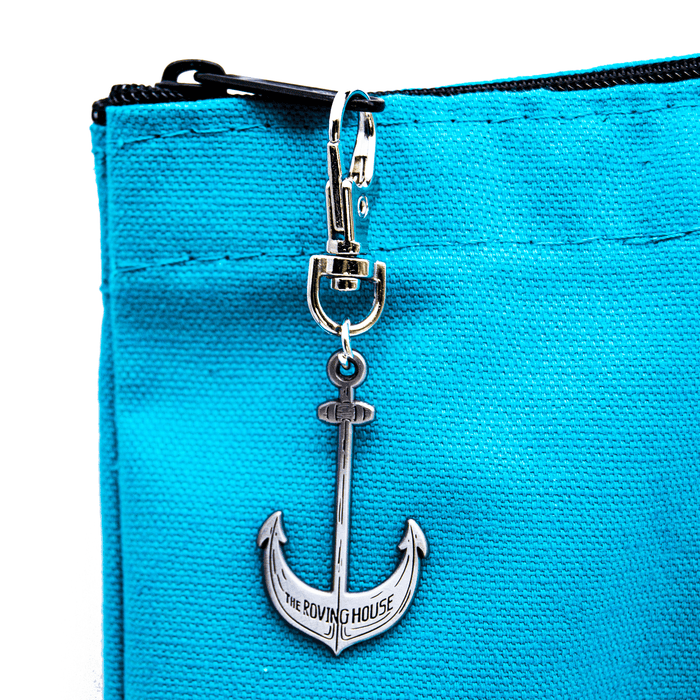 A close up of the ship's anchor shaped zipper pull on the turquoise tote bag. Small text on the anchor reads "The Roving House".