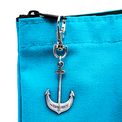 A close up of the ship's anchor shaped zipper pull on the turquoise tote bag. Small text on the anchor reads "The Roving House".