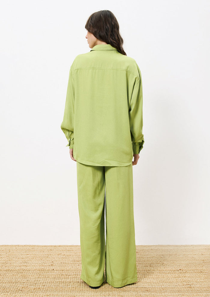 A woman wearing a button front shirt in green with double button flap pocket detail at chest.