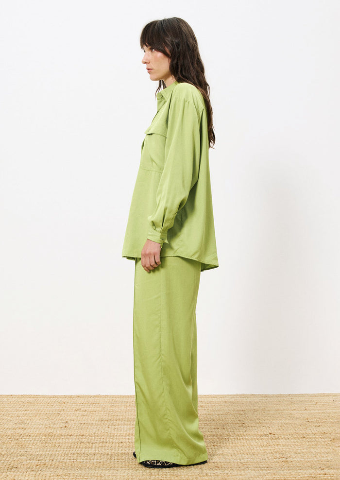 A woman wearing a button front shirt in green with double button flap pocket detail at chest.