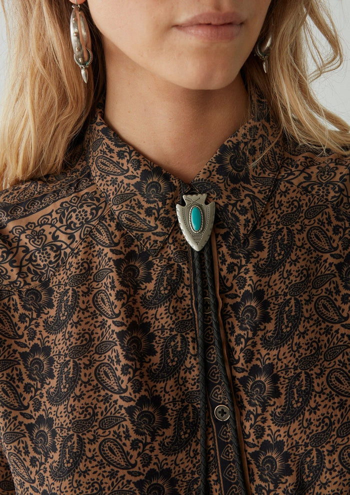 A woman wearing a paisley print blouse in brown and black.