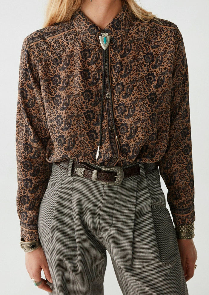 A woman wearing a paisley print blouse in brown and black.