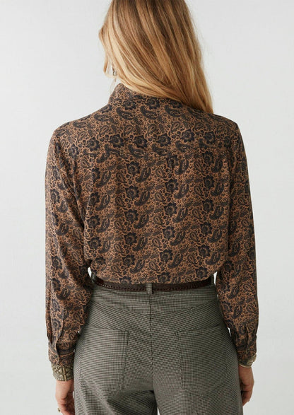 A woman wearing a paisley print blouse in brown and black.