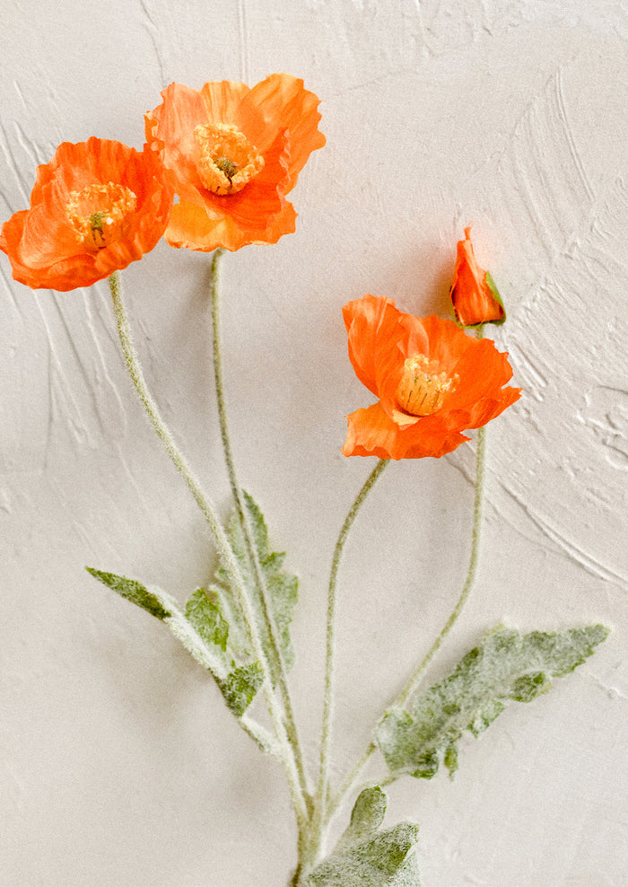 A faux floral stem depicting icelandic poppy flower in bright orange color.