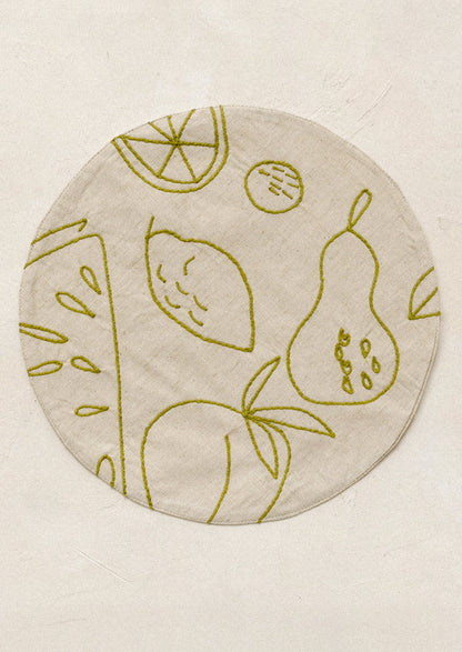 Round placemat with embroidered fruit design in green.