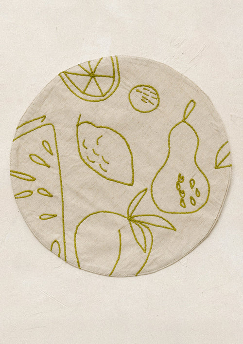 Round placemat with embroidered fruit design in green.
