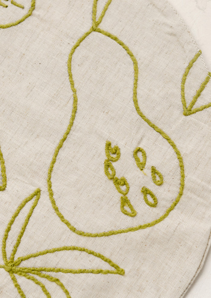 Round placemat with embroidered fruit design in green.