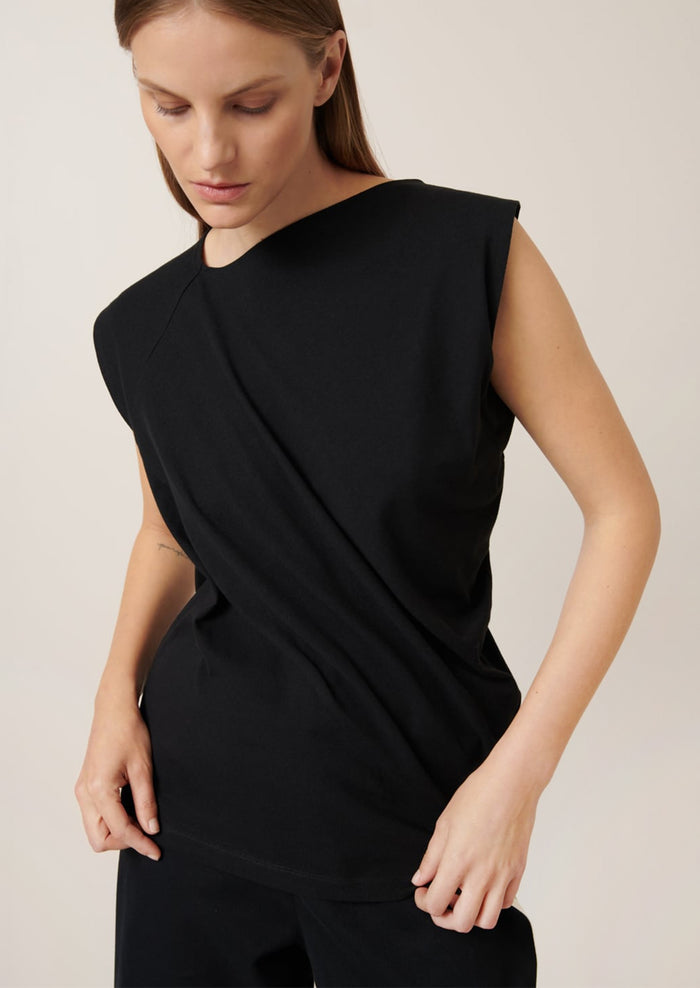 A woman wearing a black cap sleeve t-shirt with drape front detail.