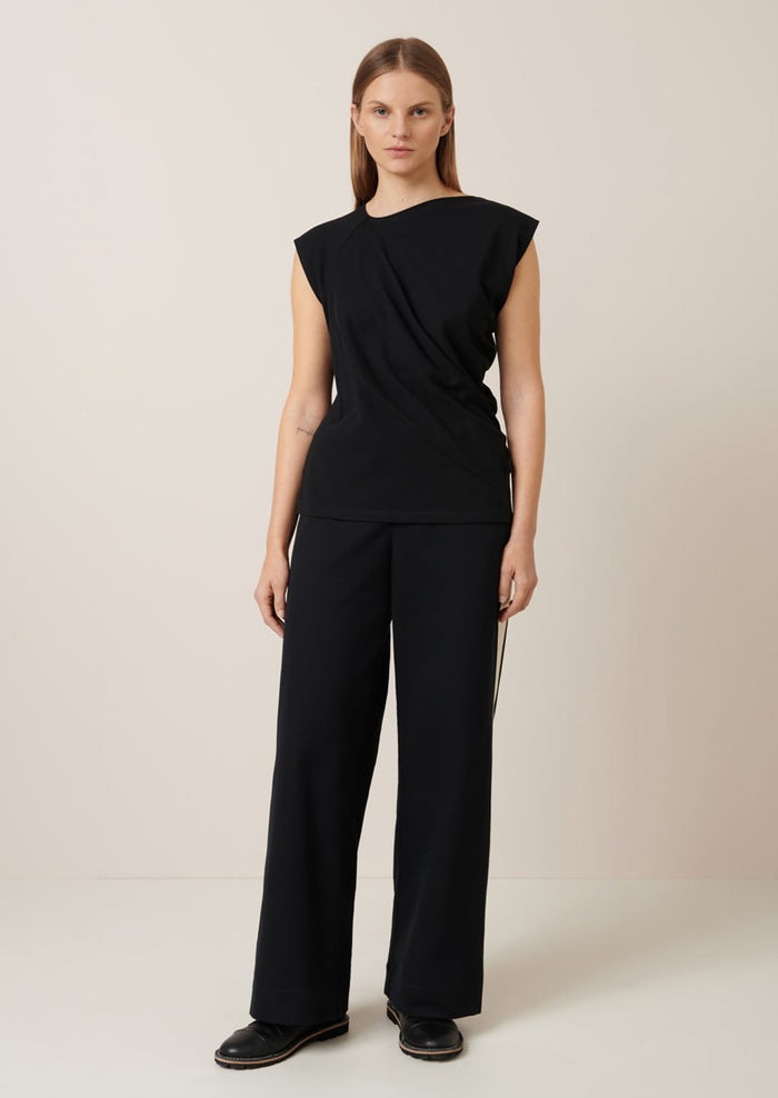 A woman wearing a black cap sleeve t-shirt with drape front detail.