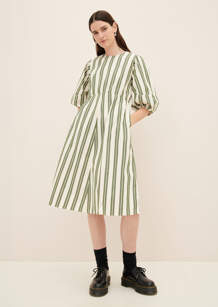 A woman wearing a cream dress with double wide vertical striping in forest green.