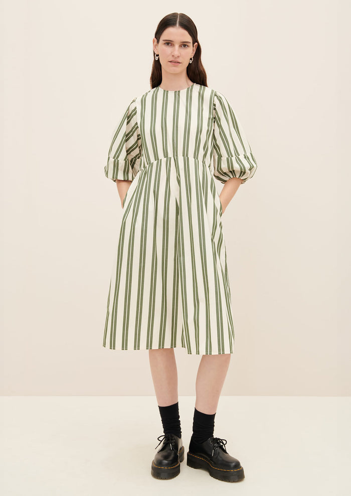 A woman wearing a cream dress with double wide vertical striping in forest green.
