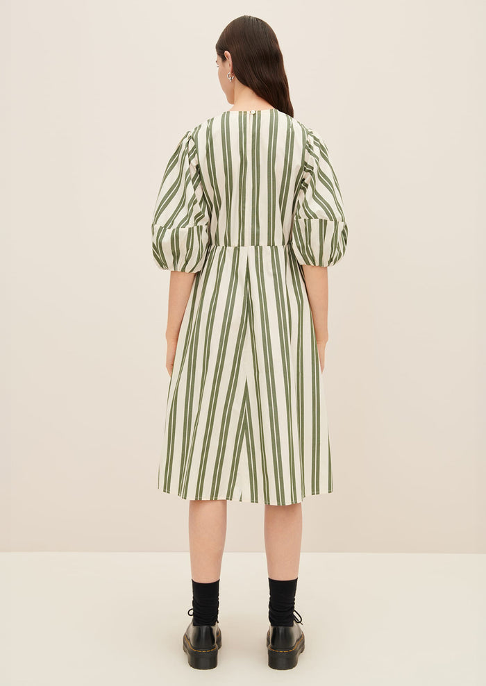 A woman wearing a cream dress with double wide vertical striping in forest green.