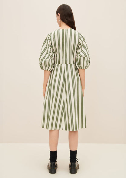 A woman wearing a cream dress with double wide vertical striping in forest green.