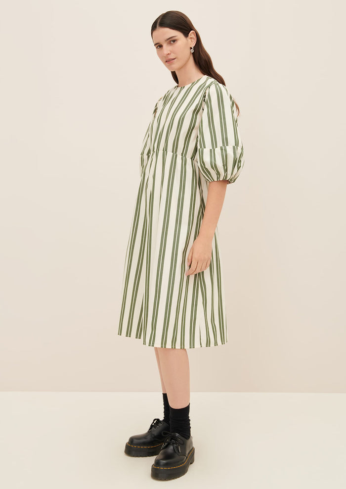 A woman wearing a cream dress with double wide vertical striping in forest green.