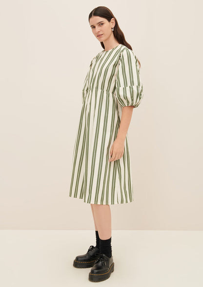 A woman wearing a cream dress with double wide vertical striping in forest green.