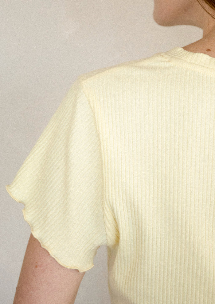 A woman wearing a yellow short sleeve baby tee with ruffled sleeve and hem.