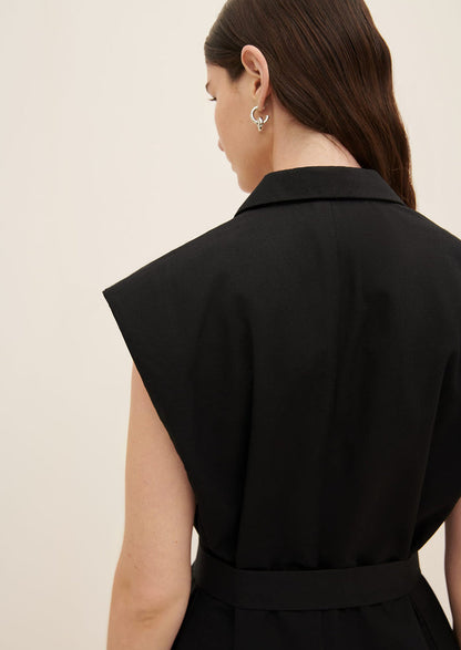 A woman wearing a black sleeveless blazer vest, with padded cap sleeve shoulders.