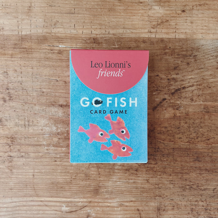 Leo Lionni's Go Fish Card Game box, front view, teal and coral design with illustrated pink fish, flat lay on rustic wooden surface