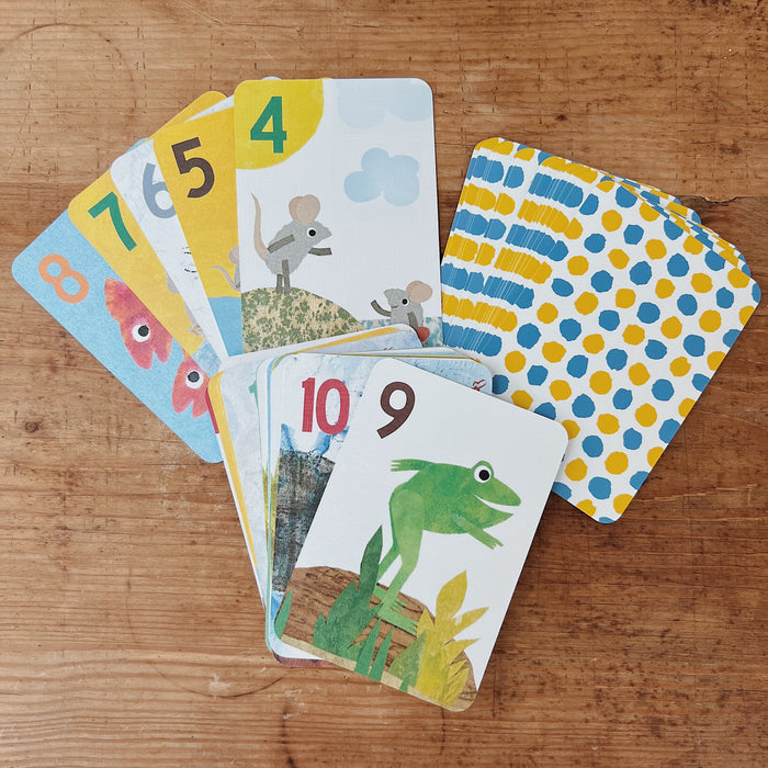 Leo Lionni's Go Fish Card Game cards fanned out on rustic wooden surface, showing colorful illustrated characters including a frog, mice, and fish, with patterned card backs in yellow and blue