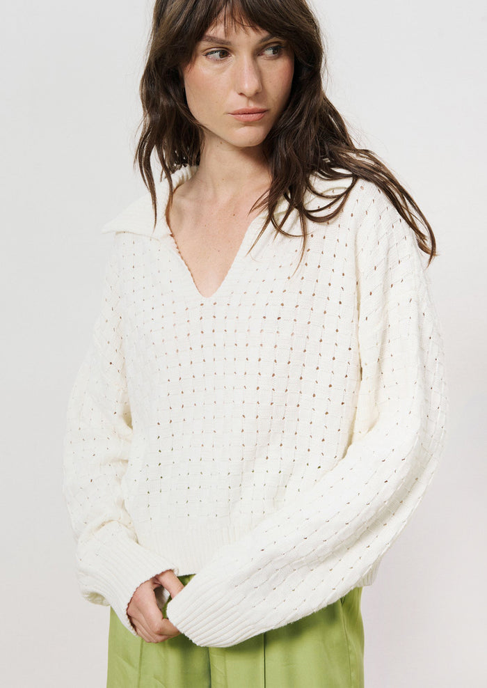 A woman wearing a collared v-neck sweater with woven texture in white.