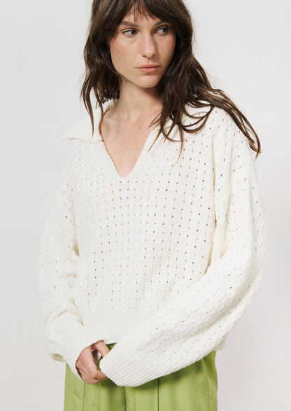 A woman wearing a collared v-neck sweater with woven texture in white.