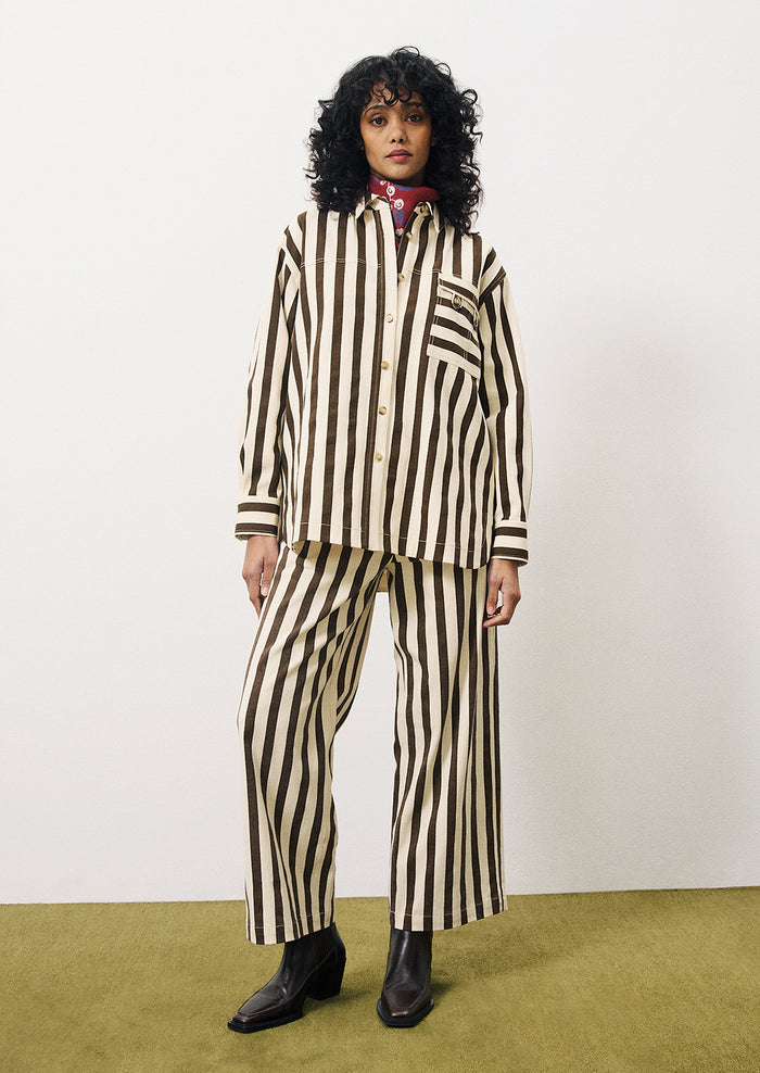 A woman wearing a cargo style button up shirt with vertical thick dark brown stripes on cream.