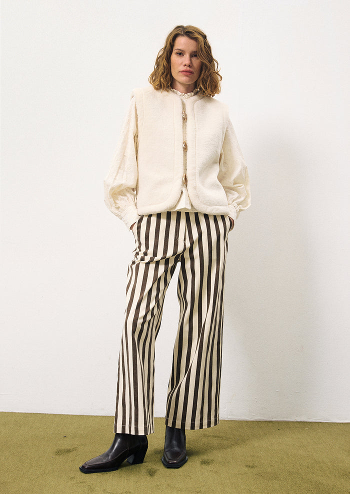 A woman wearing a pair of pants with thick vertical brown stripes on cream.