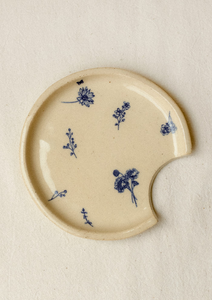 An ivory ceramic spoon rest with delicate blue floral pattern.