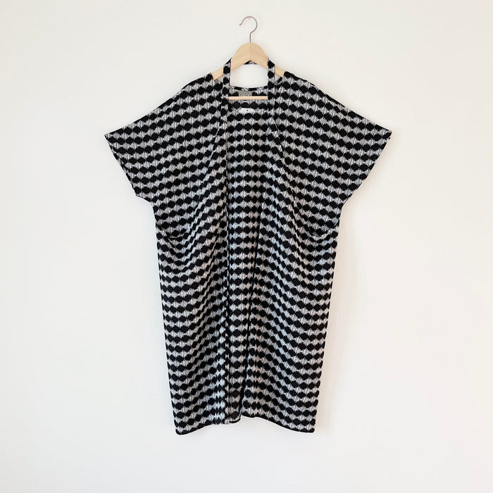 A black and white checkered origami dress hanging on a wooden hanger against a white wall.