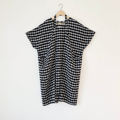 A black and white checkered origami dress hanging on a wooden hanger against a white wall.
