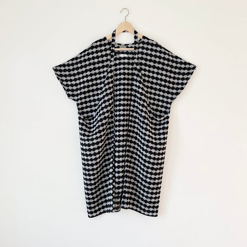 A black and white checkered origami dress hanging on a wooden hanger against a white wall.
