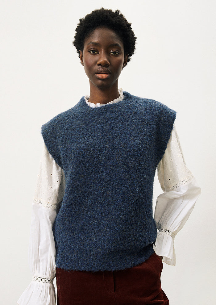 A woman wearing a cap sleeve sweater vest in marled blue knit with boucle texture.