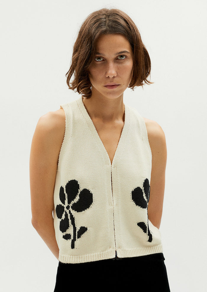 A woman wearing a sleeveless v-neck top in cream with black jacquard flower pattern.