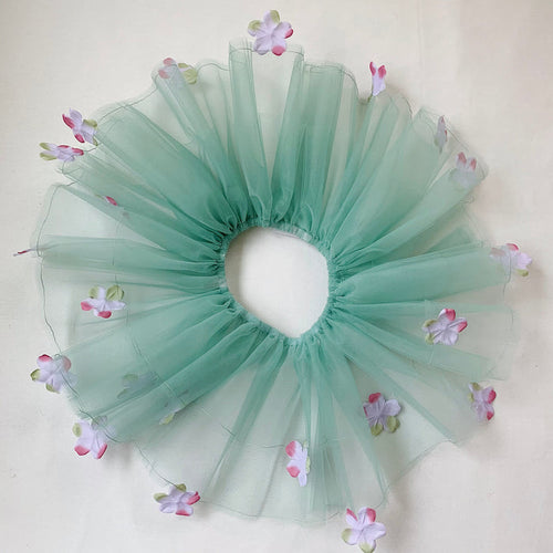 A sage green tutu with lavender colored flowers and an elastic waistband, displayed on a neutral background.
