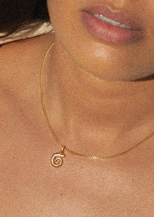 Gold necklace with a spiral pendant on a person's neck